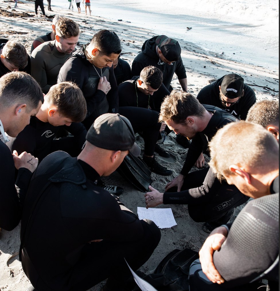 A group in wetsuits huddled on the beach during an Operation Resilience session